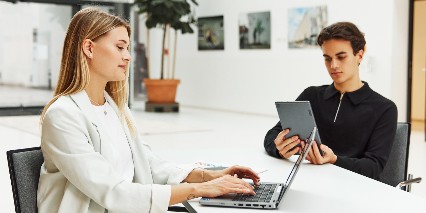 Zwei junge Personen sitzen in der Promenadengalerie und arbeiten an Laptop und Tablet mit der O&Ouml;Nachrichten Zeitung neben ihnen